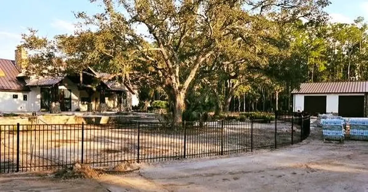 Black aluminum fence following a curved dirt road on an Orlando property