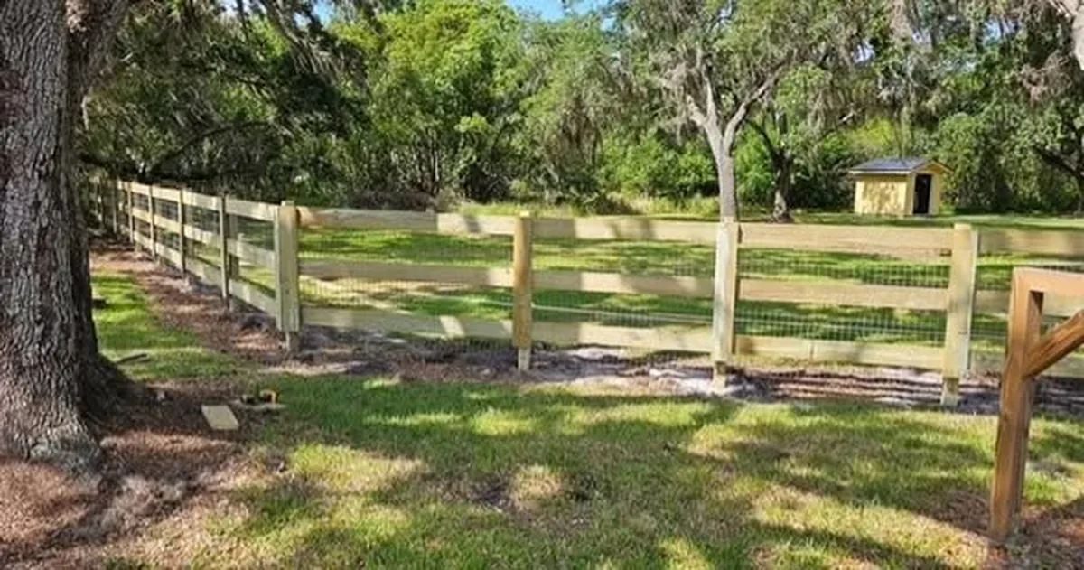 Three rail wood fence with wire backing running along a Winter Park field