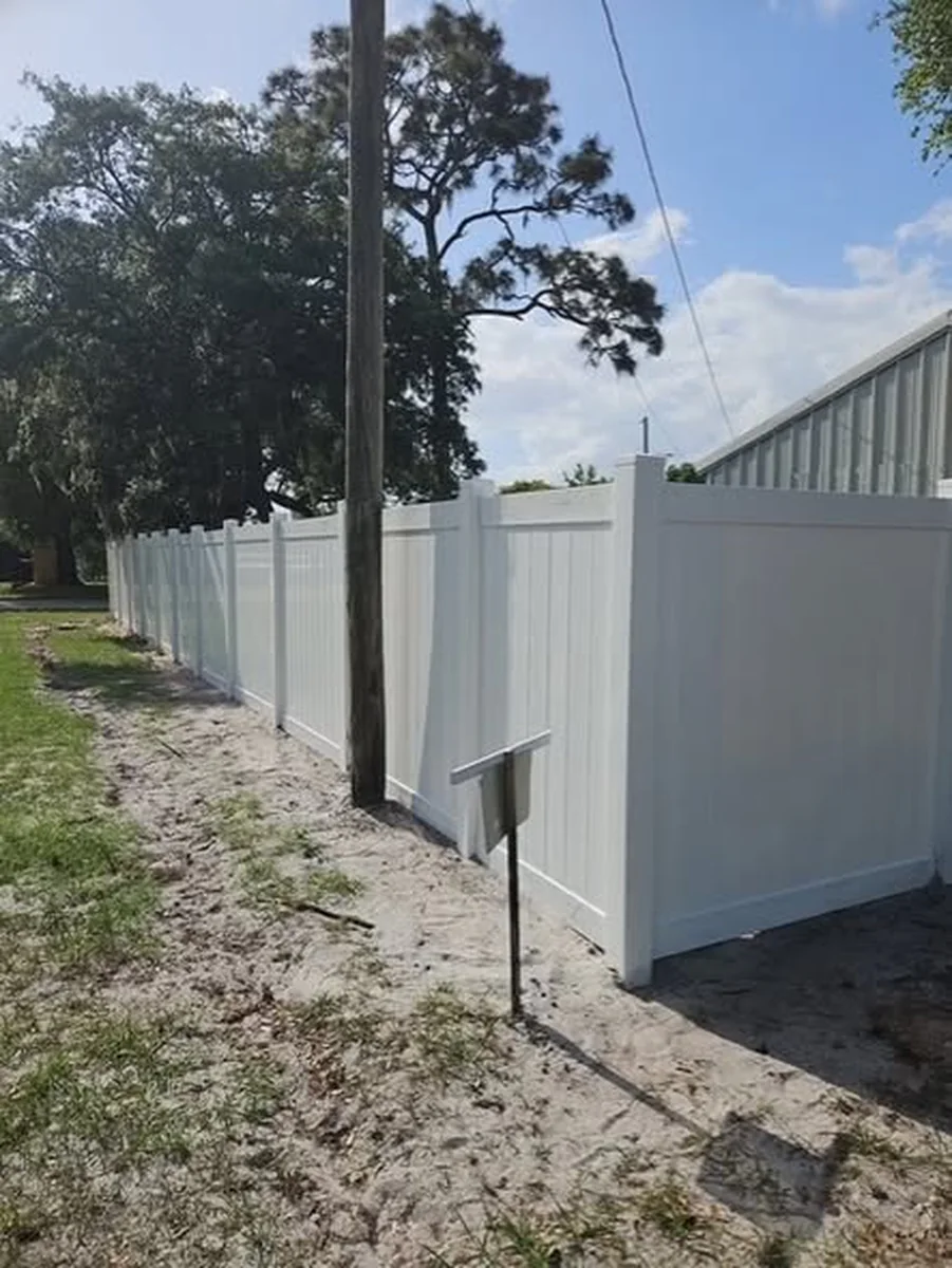 White vinyl privacy fence set in sandy ground along a commercial lot in Orlando